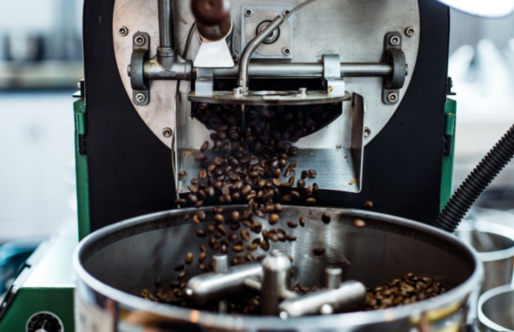 Kaffeebohnen fallen in einen großen Metallkessel.