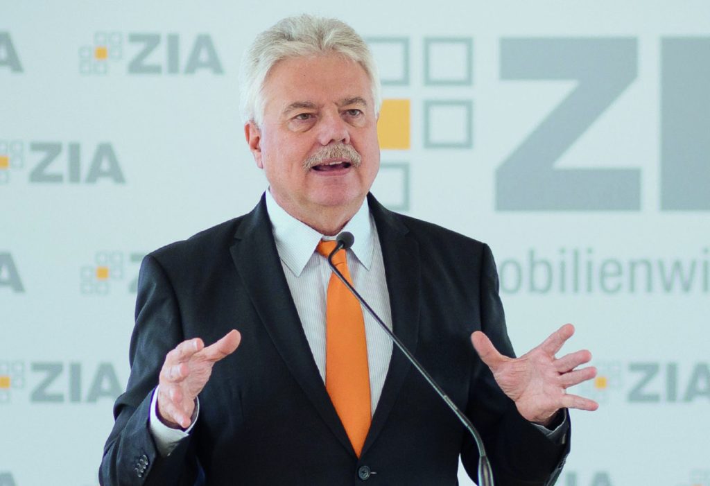 Andreas Mattner trägt einen schwarzen Anzug, ein weißes Hemd und eine orangene Krawatte. Erneuerbare Energien einbringen. 