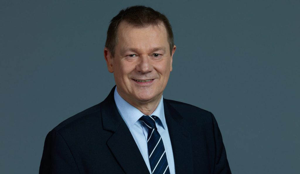 Markus Pieper, parlamentarischer Geschäftsführer der CDU/CSU im EU-Parlament und Berichterstatter für die Erneuerbare-Energien-Richtlinie, steht im Anzug vor einem grauen Hintergrund. 