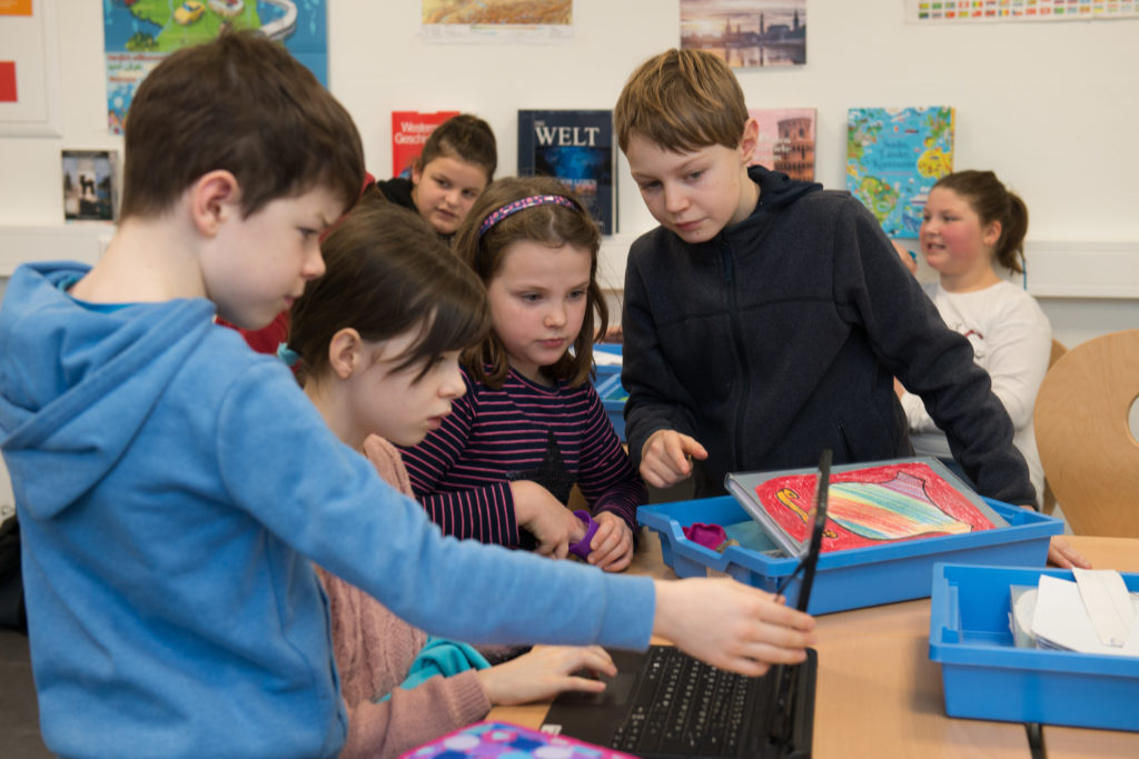 Man sieht eine Gruppe Kinder an einem Tisch, sie sehen wie künstliche Intelligenz in der Reformschule eingesetzt wird.