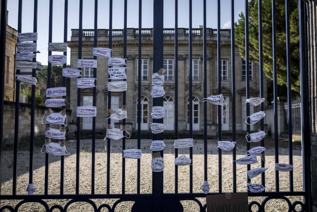 Man sieht ein Tor vor einem Gebäude auf dem OP-Masken hängen: Proteste für Distanzunterricht in Frankreich, es funktioniert für Lehrer