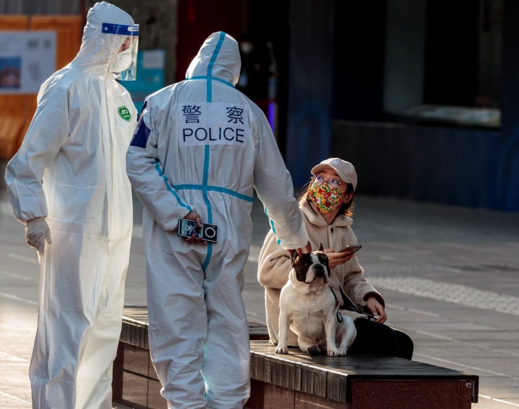 Shanghai police in protective suits interacting with a woman on a bench