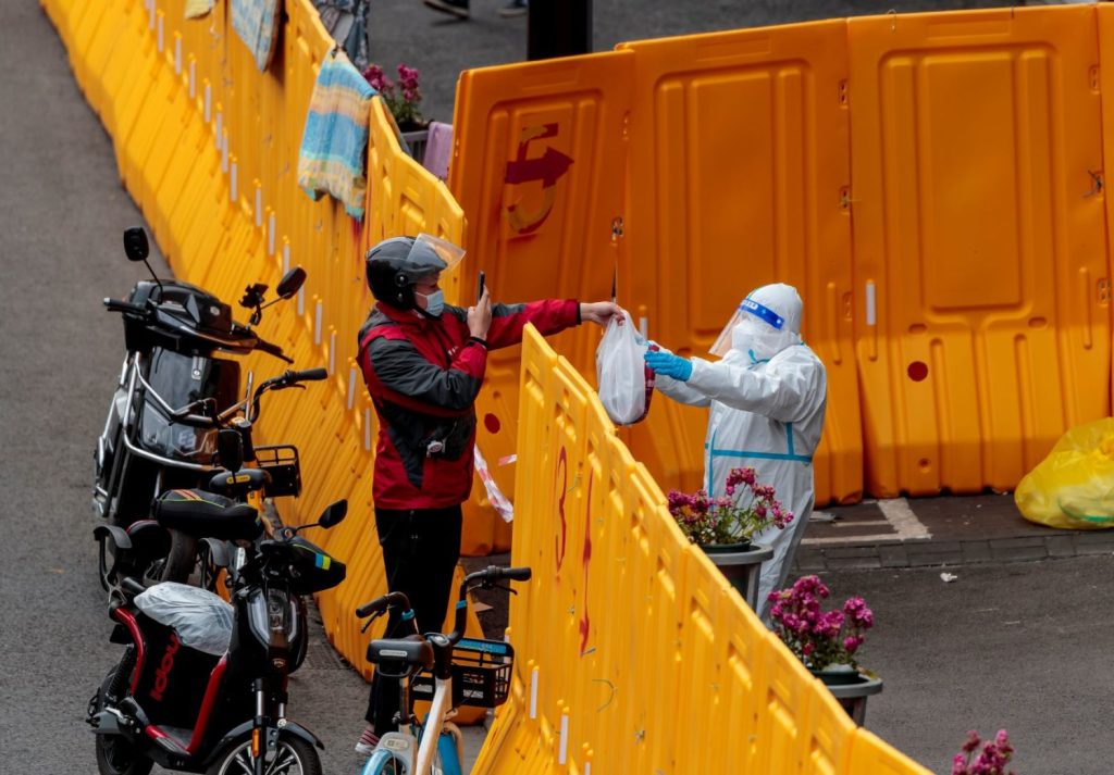 Delivery driver handing food over an orange barricade to a worker in protective gear