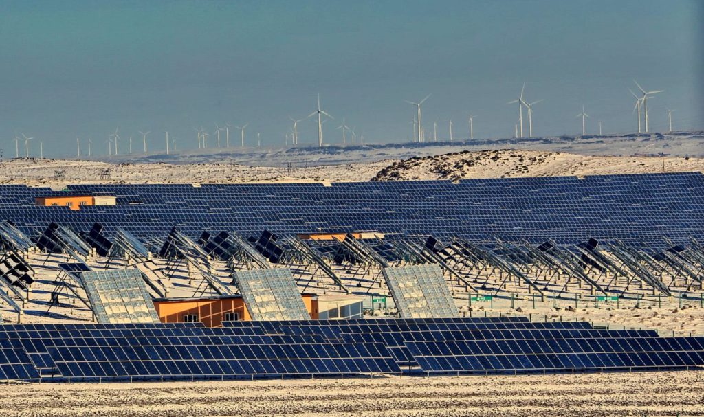 Eine Fotovoltaikanlage im Winter, gelegen vor einem Bergrücken vollerWindräder