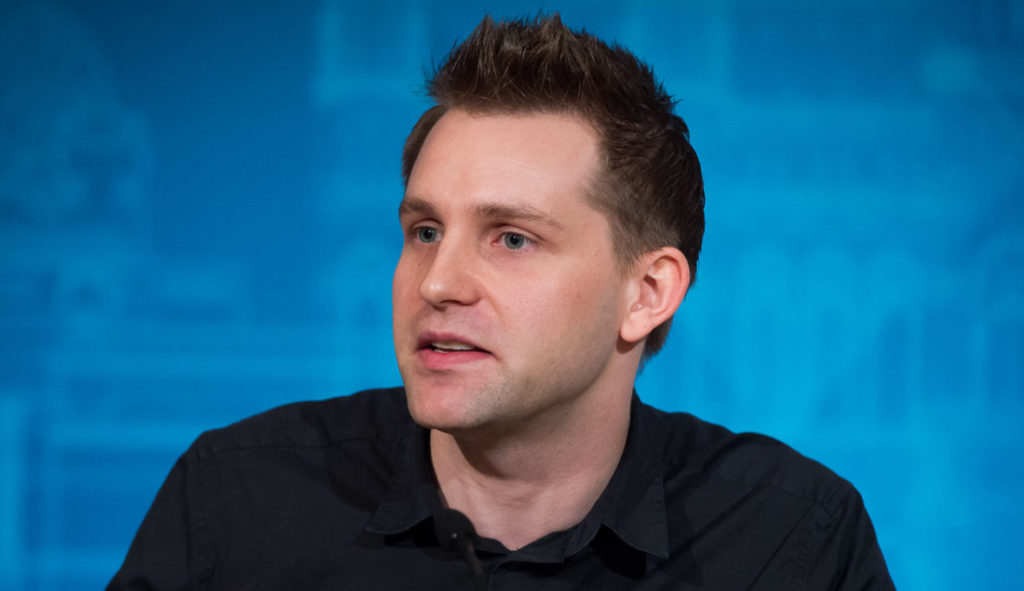 Man sieht Max Schrems vor einer blauen Wand, er setzt sich für Datenschutz ein.