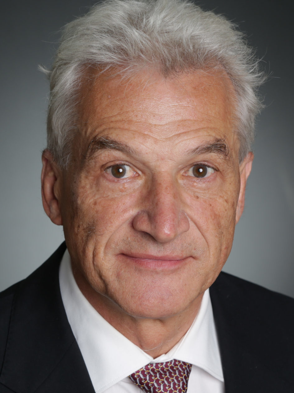 Porträtfoto von Volker Stanzel in einem Anzug vor grauem Hintergrund. 