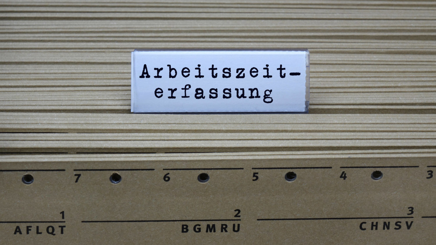 Man sieht einen Ordner voller Akten auf dem eine Schild steht mit dem Wort Arbeitszeiterfassung: Soll die Erfassung von Arbeitszeit nun auch für Lehrer ermöglicht werden?