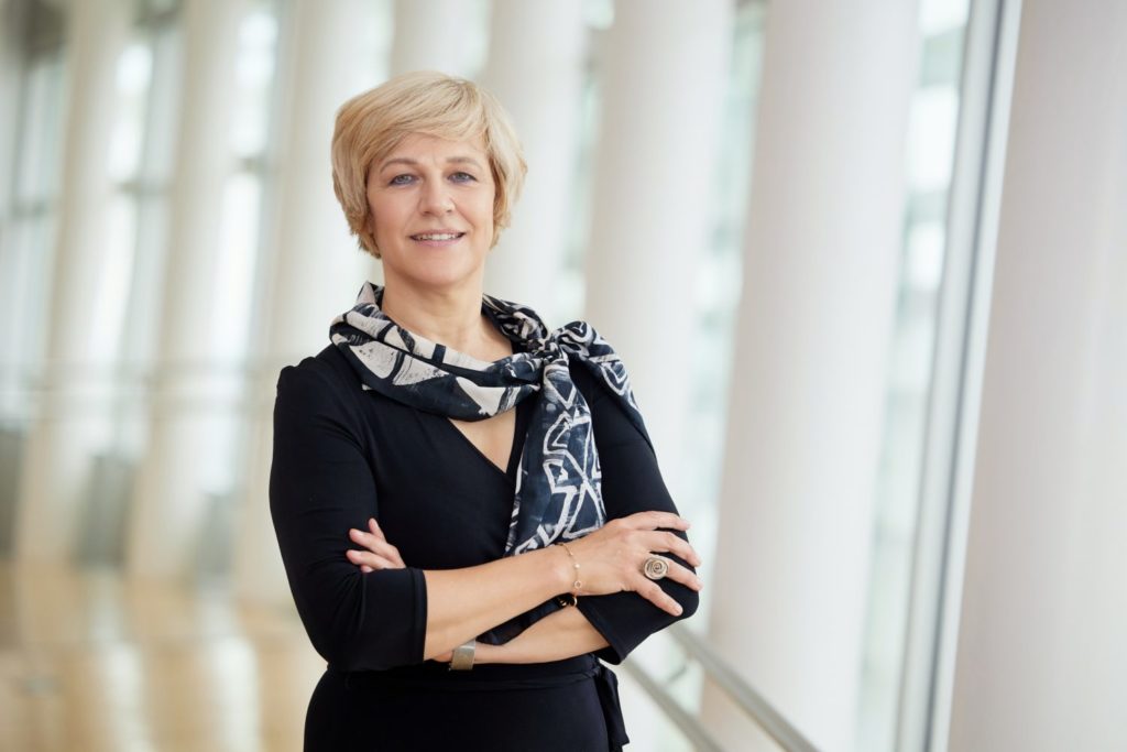 Porträtfoto von Renate Nikolay, neue stellvertretende Generaldirektorin der GD Connect, mit verschränkten Armen und Schal vor einer Fensterfront. 