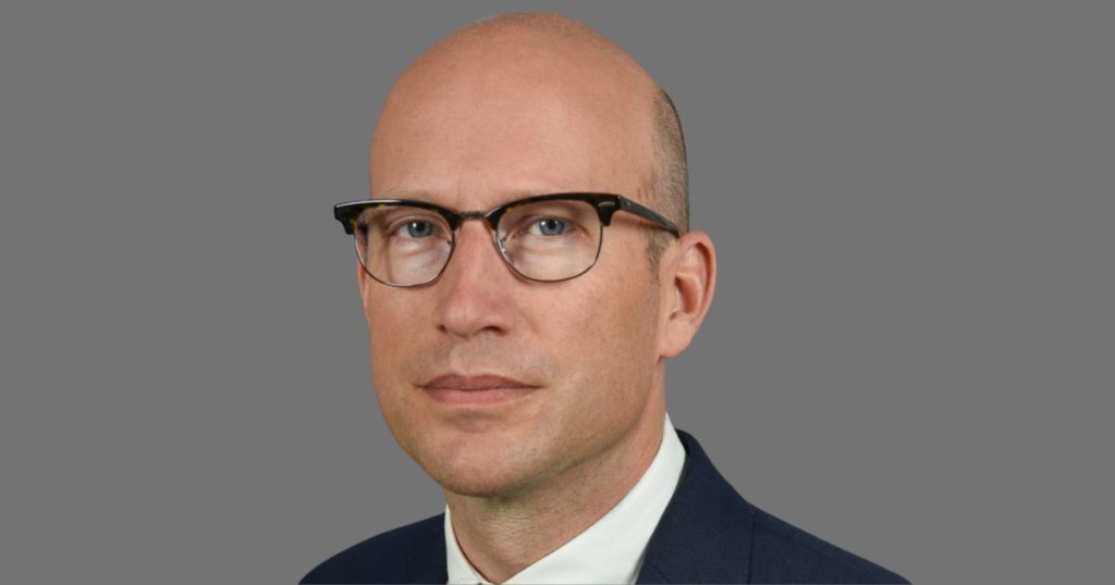 Porträtfoto von Sven Rösner im Anzug vor grauem Hintergrund. 