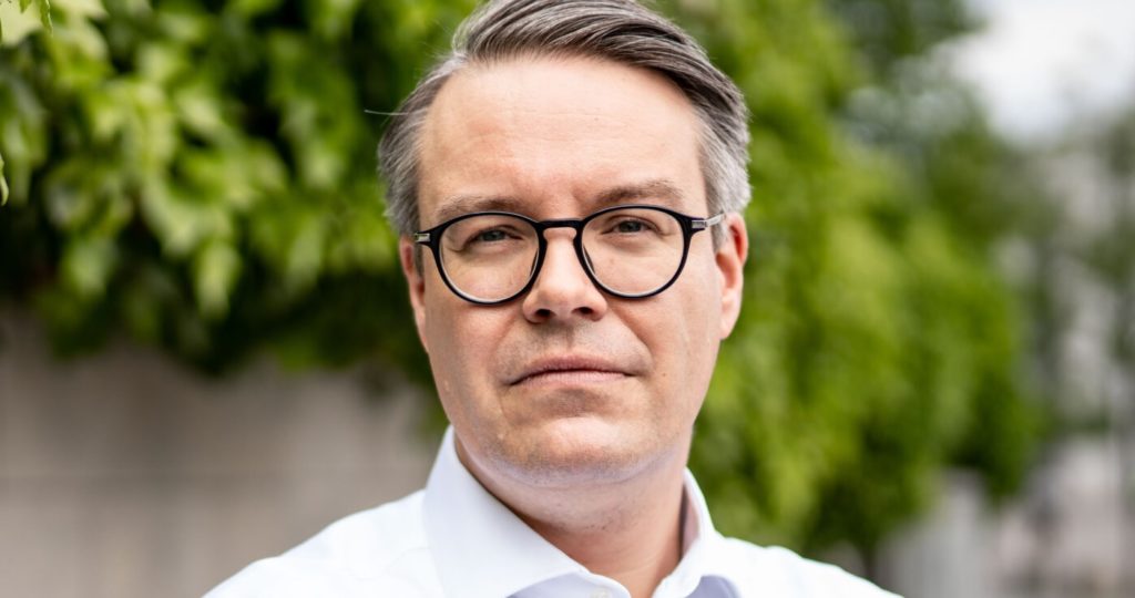 Porträtfoto von Tobias Lindner (Grüne) mit einer Brille vor Grün. 