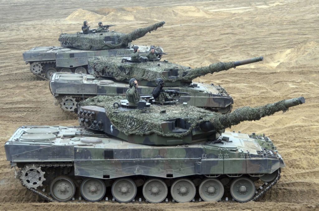 Abbildung von drei Leopard 2A4 Panzern des polnischen Militärs auf sandigem Untergrund.