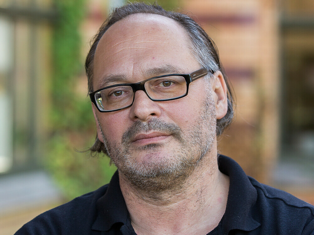 Porträtfoto eines Mannes im schwarzen Poloshirt und mit Brille