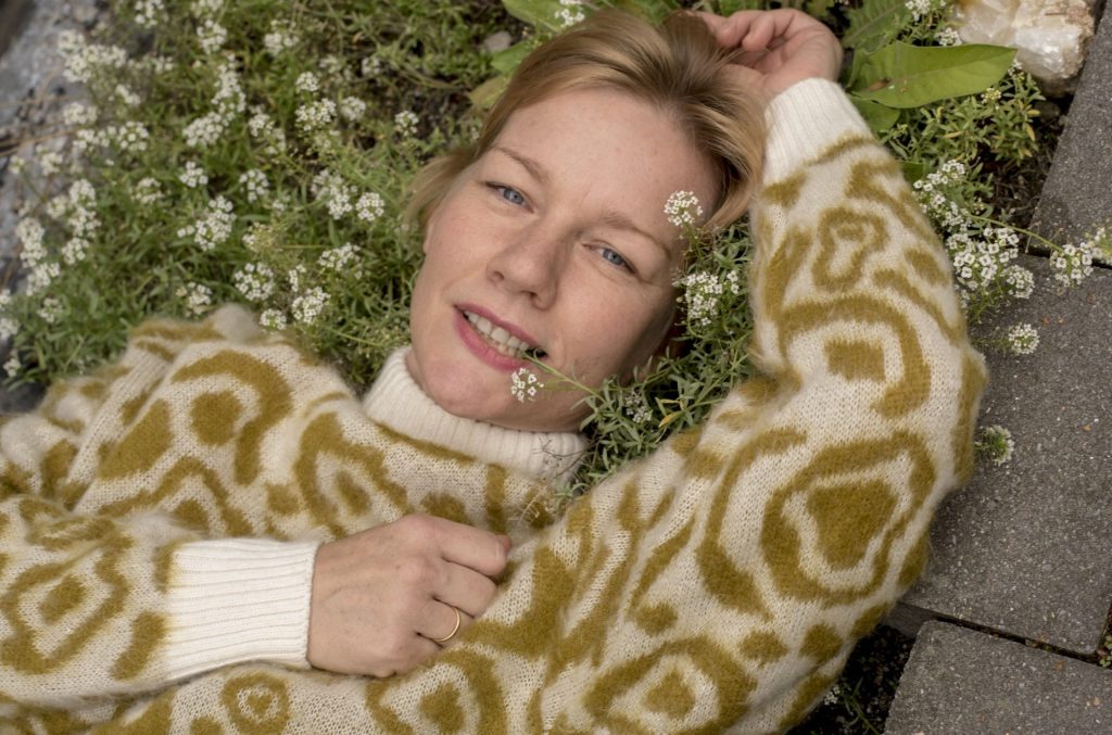 Sandra Hüller, liegend in einem Beet mit weiß blühenden Blumen