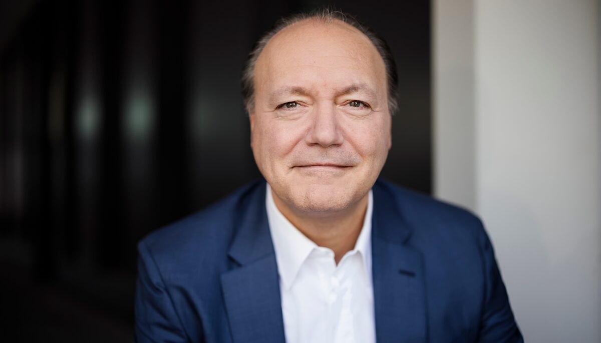 Ein Foto von Marc Reinhardt, er lächelt leicht in die Kamera, hat eine Halbglatze und trägt ein dunkelblaues Jackett