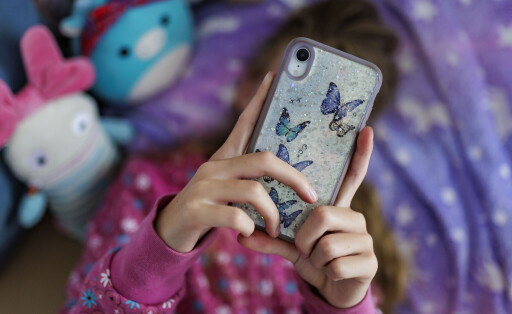 Ein Maedchen liegt in ihrem Bett und ist am Handy.