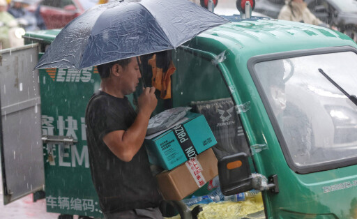 19.08.2025 Ein Paketlieferant liefert trotz Flutwarnung der Stufe 3 für Peking weiter aus.