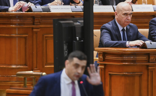 Romanian Prime Minister Ilie Bolojan, top right, looks on as George Simion, leader of the opposition right wing AUR alliance, addresses a parliament session ahead of a no confidence vote initiated by opposition parties attempting to block fiscal measures by the government aiming to reduce the country's budgetary deficit in Bucharest, Romania, Monday, July 14, 2025.