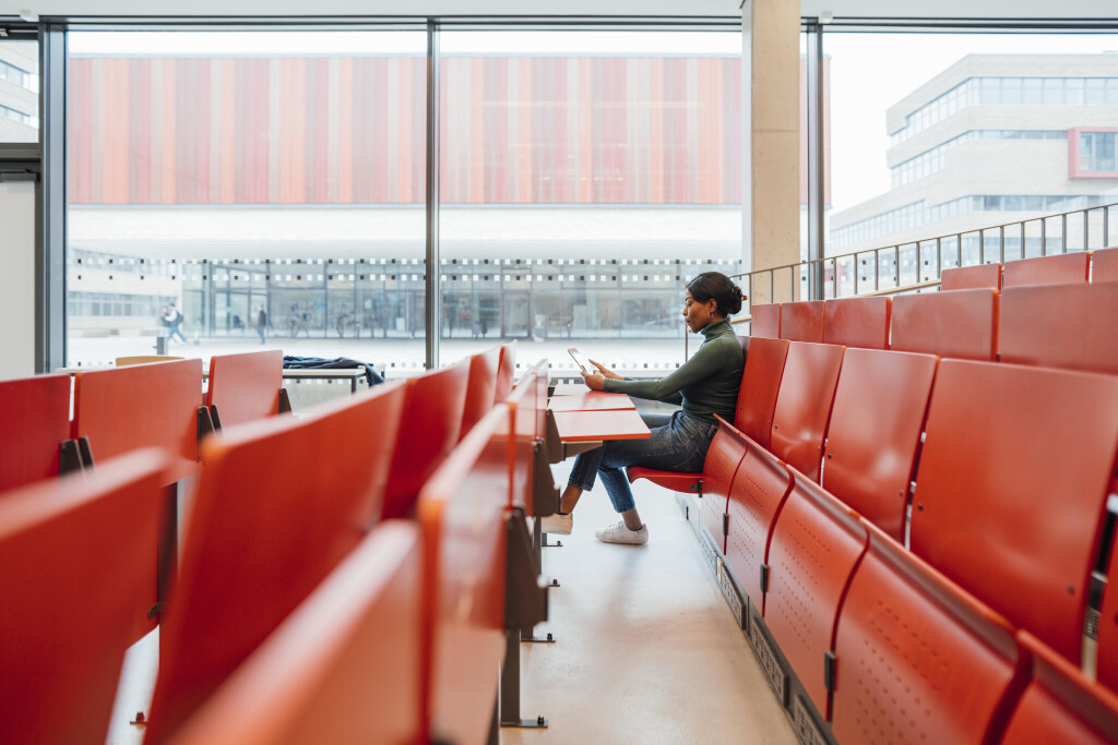 Young woman working on tablet PC sitting on seat in auditorium