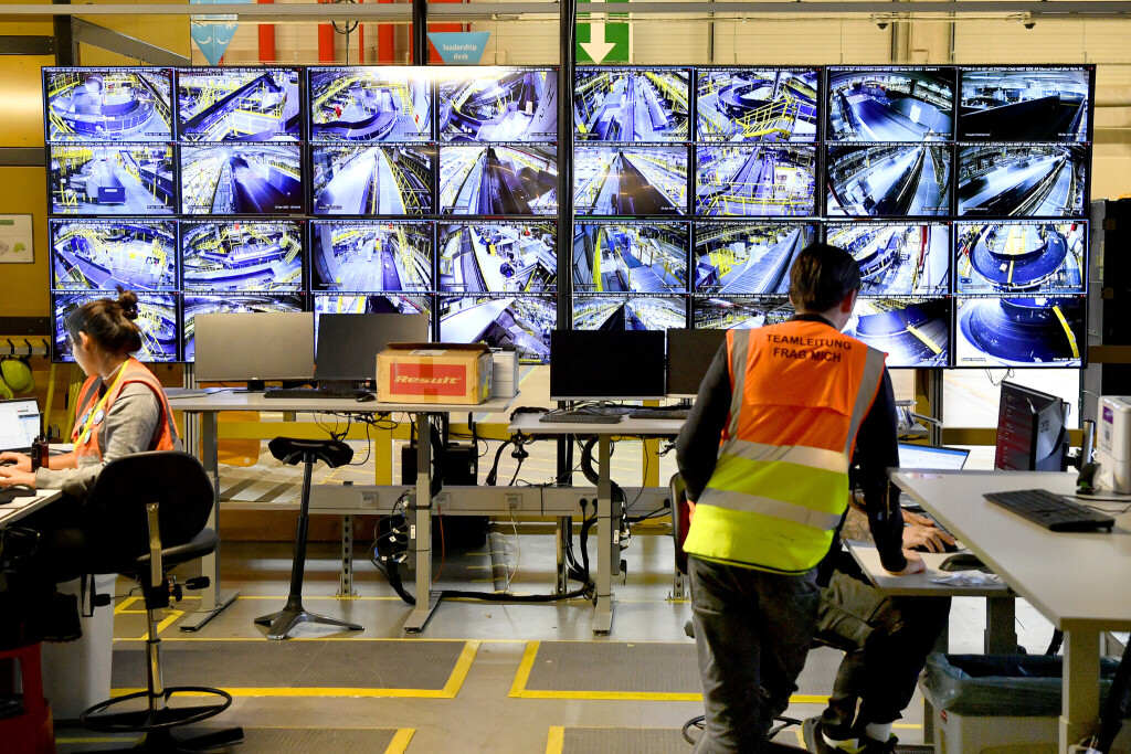 Eine Frau mit der Weste "Teamleitung" steht vor einer Reihe von Monitoren, die die Arbeit im Sortierzentrum von Amazon in Witten überwachen.