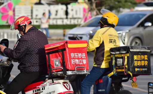 Fahrer von JD Takeaway (L), dem Essenslieferdienst des chinesischen E-Commerce-Giganten JD.com, und Meituan (R) warten am 23. April 2025 in Shenyang, Provinz Liaoning, auf grünes Licht für die Fahrt.