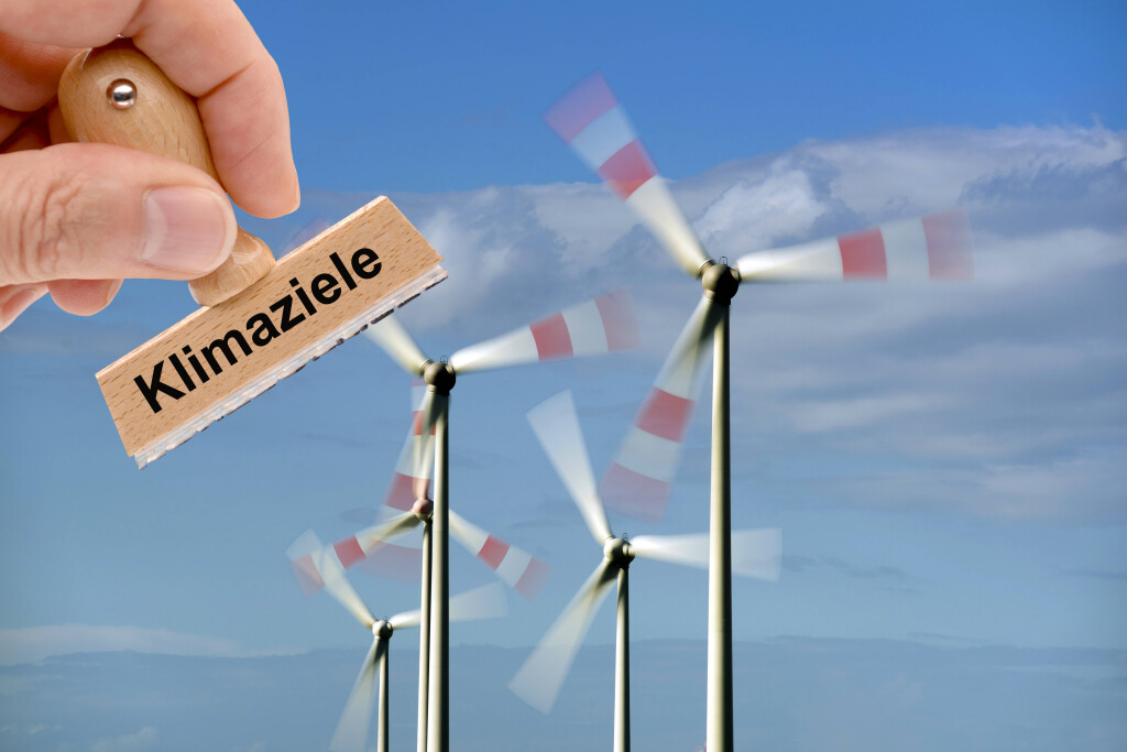 Windkraftanlage für das Erreichen der Klimaziele Ein Holzstempel ist beschriftet mit dem Aufdruck Klimaziele und wird von einer Hand vor eine Windkraftanlage mit drehenden Rotorblättern gehalten - FOTOMONTAGE *** Wind turbine for achieving the climate targets A wooden stamp is labeled with the words climate targets and is held by a hand in front of a wind turbine with rotating rotor blades FOTOMONTAGE