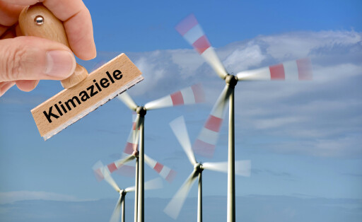 Windkraftanlage für das Erreichen der Klimaziele Ein Holzstempel ist beschriftet mit dem Aufdruck Klimaziele und wird von einer Hand vor eine Windkraftanlage mit drehenden Rotorblättern gehalten - FOTOMONTAGE *** Wind turbine for achieving the climate targets A wooden stamp is labeled with the words climate targets and is held by a hand in front of a wind turbine with rotating rotor blades FOTOMONTAGE