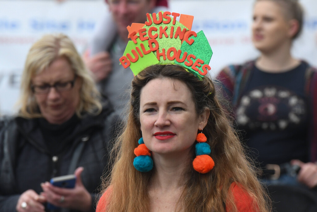 Eine Demonstrantin in Dublin mit einem schild auf dem Kopf auf dem steht "Just fecking build houses"