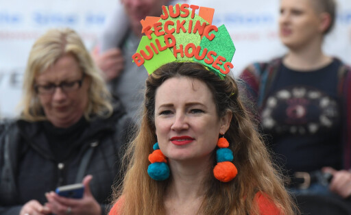 Eine Demonstrantin in Dublin mit einem schild auf dem Kopf auf dem steht "Just fecking build houses"