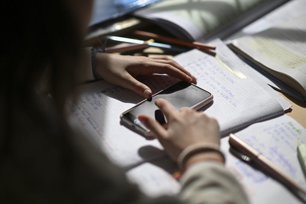 Ein Mädchen tippt auf ein Smartphone, das auf einem Schulheft liegt.