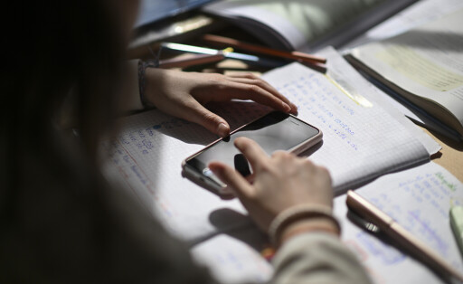 Ein Mädchen tippt auf ein Smartphone, das auf einem Schulheft liegt.