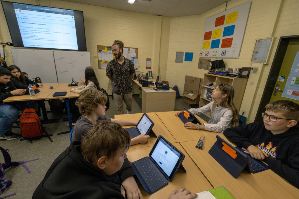 Schüler sitzen in einem Klassenzimmer an ihren Plätzen und schauen auf Tablets, die auf ihren Tischen stehen.