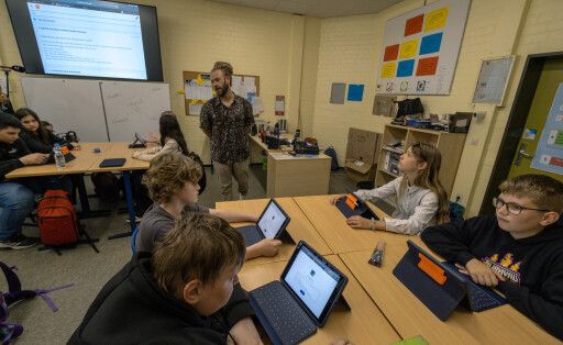Schüler sitzen in einem Klassenzimmer an ihren Plätzen und schauen auf Tablets, die auf ihren Tischen stehen.