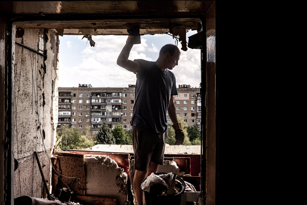 Das Bild zeigt einen Mann vor einem zerstörten Fenster in seiner Wohnung. Russische Angreifer zielen immer wieder auf zivile Objekte in der Ukraine.