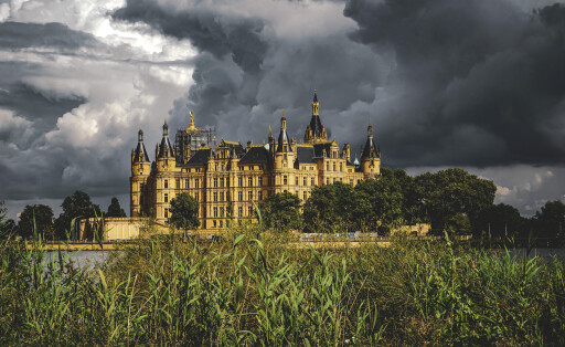 Hinter dem sandsteinfarbenen Schloss Schwerin ziehen dunkle Wolken am Himmel zusammen.
