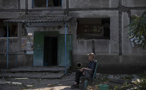 Das Bild zeit einen alten Mann, der vor einem zerstörten mehrgeschossigen Gebäude im ukrainischen Ort Dobropillja sitzt.