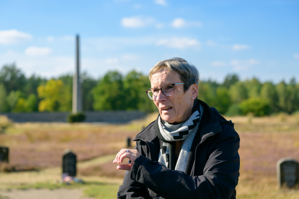 Elke Gryglewski steht sprechend auf einem Friedhof.
