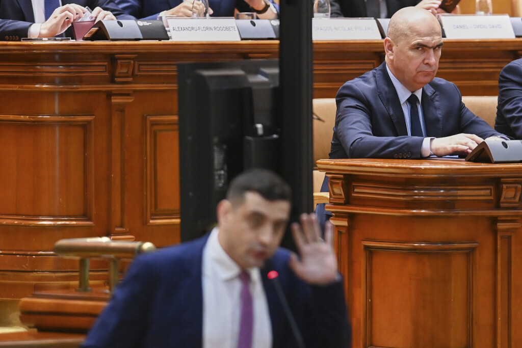 Romanian Prime Minister Ilie Bolojan, top right, looks on as George Simion, leader of the opposition right wing AUR alliance, addresses a parliament session ahead of a no confidence vote initiated by opposition parties attempting to block fiscal measures by the government aiming to reduce the country's budgetary deficit in Bucharest, Romania, Monday, July 14, 2025.