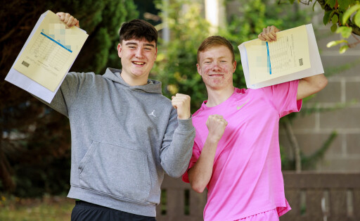 Zwei Schüler halten ihr Zeugnis hoch und freuen sich.