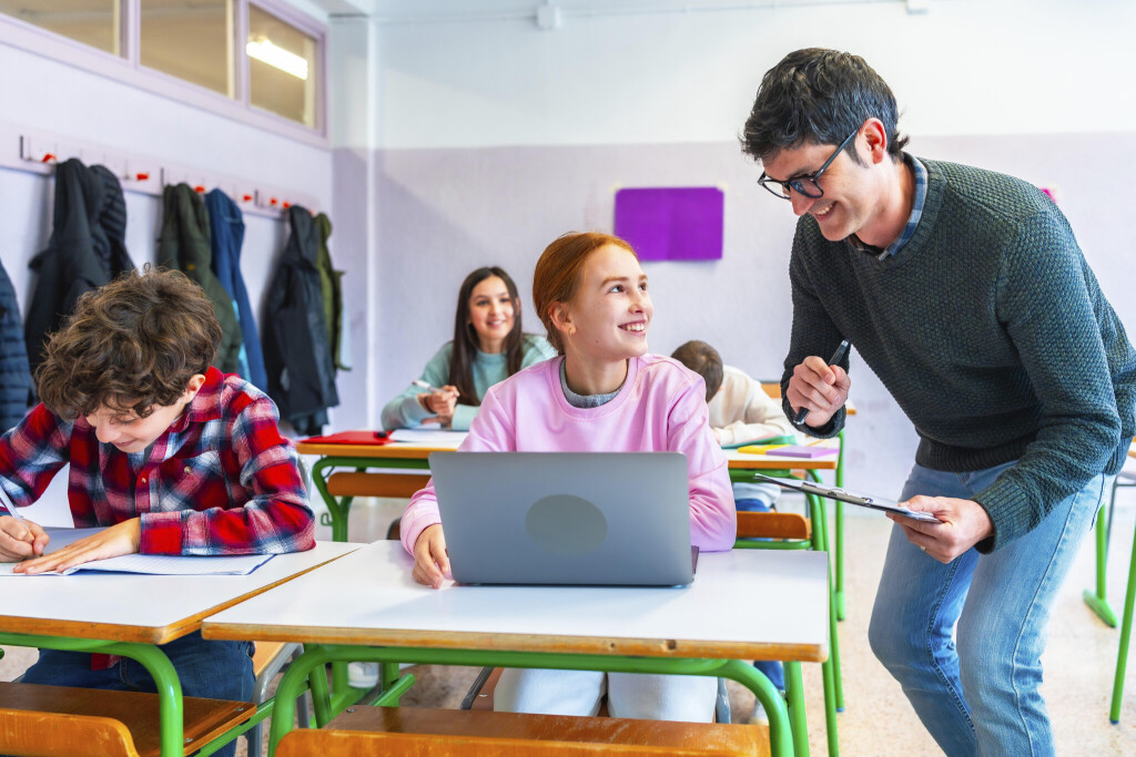 Grundschüler arbeiten in Heften, eine Schülerin arbeitet am Laptop.