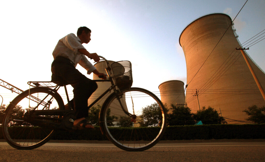 July 12, 2013, BEIJING, CHINA: A Chinese man cycles past massive water cooling towers at one of Beijing s main coal-fire