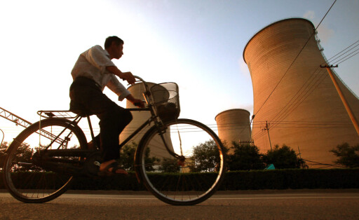 July 12, 2013, BEIJING, CHINA: A Chinese man cycles past massive water cooling towers at one of Beijing s main coal-fire