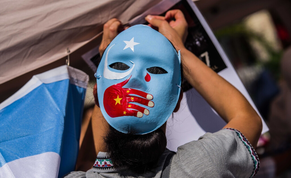 August 8, 2020, Munich, Bavaria, Germany: A demonstrator in Munich, Germany wears a mask with the Uyghur/East Turkestan flag with the Chinese flag on a hand symbolizing the oppression they face in the Xinjiang Province of China. Bringing attention to the deteriorating situation in the Xinjiang Province of China, German Uyghurs demonstrated at Munich s Marienplatz. Potentially 11 million Uyghurs live under oppression in China with 150 of the largest concerns in Europe have economic interests in the region and Uyghurs in their supply chain, such as Nike, Volkswagen, Apple, BMW, Samsung, Huawei, Sony, and others. There are some 800 Uyghurs in the exile community in Munich. Munich Germany - ZUMAb160 20200808_zbp_b160_005 Copyright: xSachellexBabbarx