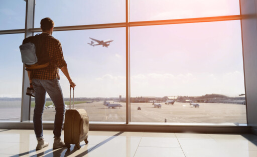 June 6, 2023: Calm male tourist is standing in airport and looking at aircraft flight through window. He is holding tickets and suitcase. Sunset - ZUMAla2_ 20230606_zaa_la2_001 Copyright: xLaxNacionx