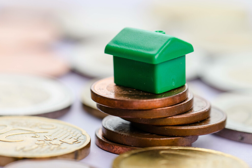 Green toy house on instable stack of coins symolizing bad economy. Green toy house on instable stack of coins symolizing bad economy Copyright: xZoonar.com/TrygvexFinkelsenx 20375460