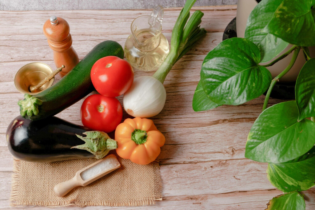 Draufsicht auf eine Gruppe der Gemüsesorten Paprika, Zwiebel, Tomate, Aubergine und Zucchini, sowie Olivenöl und Salz