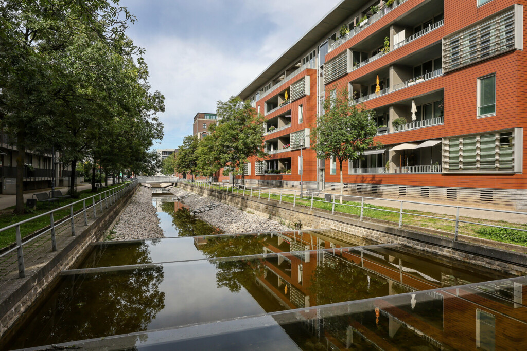Duisburg, Ruhrgebiet, Nordrhein-Westfalen, Deutschland - Schwammstadt. Klimaresiliente Stadt. Moderne Wohnhaeuser an der Speichergracht am Innenhafen Duisburg. Das künstliche Gewässer dient dem Abfluss des Niederschlagwassers von Dächern und Grundstücken in das Becken des Innenhafens und ist somit auch Teil der ökologischen Gesamtkonzeption des Innenhafens. Wasserverlust durch Verdunstung wird durch eine Grundwasserpumpe ausgeglichen, die wiederum mit Solarstrom betrieben wird. Duisburg Nordrhein-Westfalen Deutschland *** Duisburg, Ruhr Area, North Rhine-Westphalia, Germany Sponge City Climate-resilient city Modern residential buildings on Speichergracht at the Duisburg Inner Harbor The artificial body of water is used to drain precip